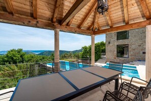 A covered outdoor area with a pool, seating, and a stone building.