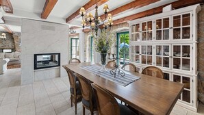 Een eethoek met een houten tafel, rieten stoelen, een kroonluchter en een stenen muur.