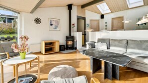 A spacious living room with a fireplace, a sofa, a coffee table, and a dining area. - 2 bedroom nice home in Juelsminde (Juelsminde)