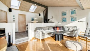 A spacious living area with a grey sofa, a round coffee table, and a wooden floor. There are skylights on the ceiling, a door leading to another room, and a wall with framed artwork. - 2 bedroom nice home in Juelsminde (Juelsminde)