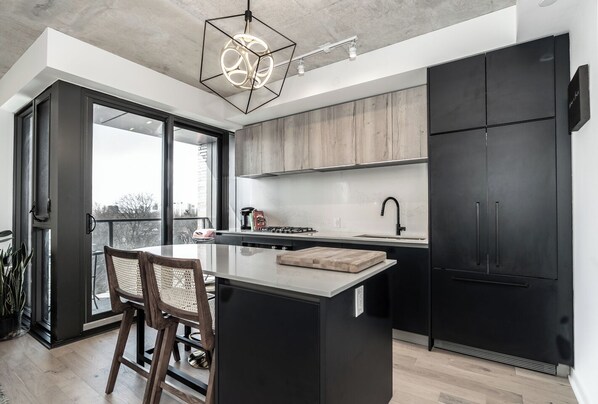 Una cocina moderna con una isla central, armarios negros y un ventanal con vistas a la ciudad.