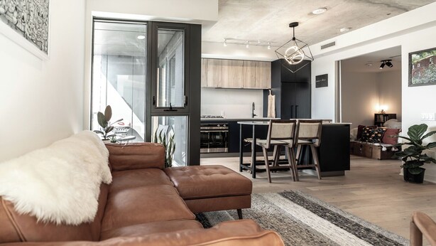 Una sala de estar moderna con un sofá de cuero marrón, un comedor con sillas de madera y una cocina al fondo.