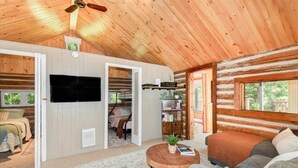 A log cabin interior with a TV, a cozy seating area, and a bookshelf. - Waterfront 3-Bedroom Cottage with Hot Tub, Fire Pit, Kayaks (Ontario)