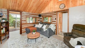 A log cabin interior with a sofa, armchair, and coffee table. - Waterfront 3-Bedroom Cottage with Hot Tub, Fire Pit, Kayaks (Ontario)