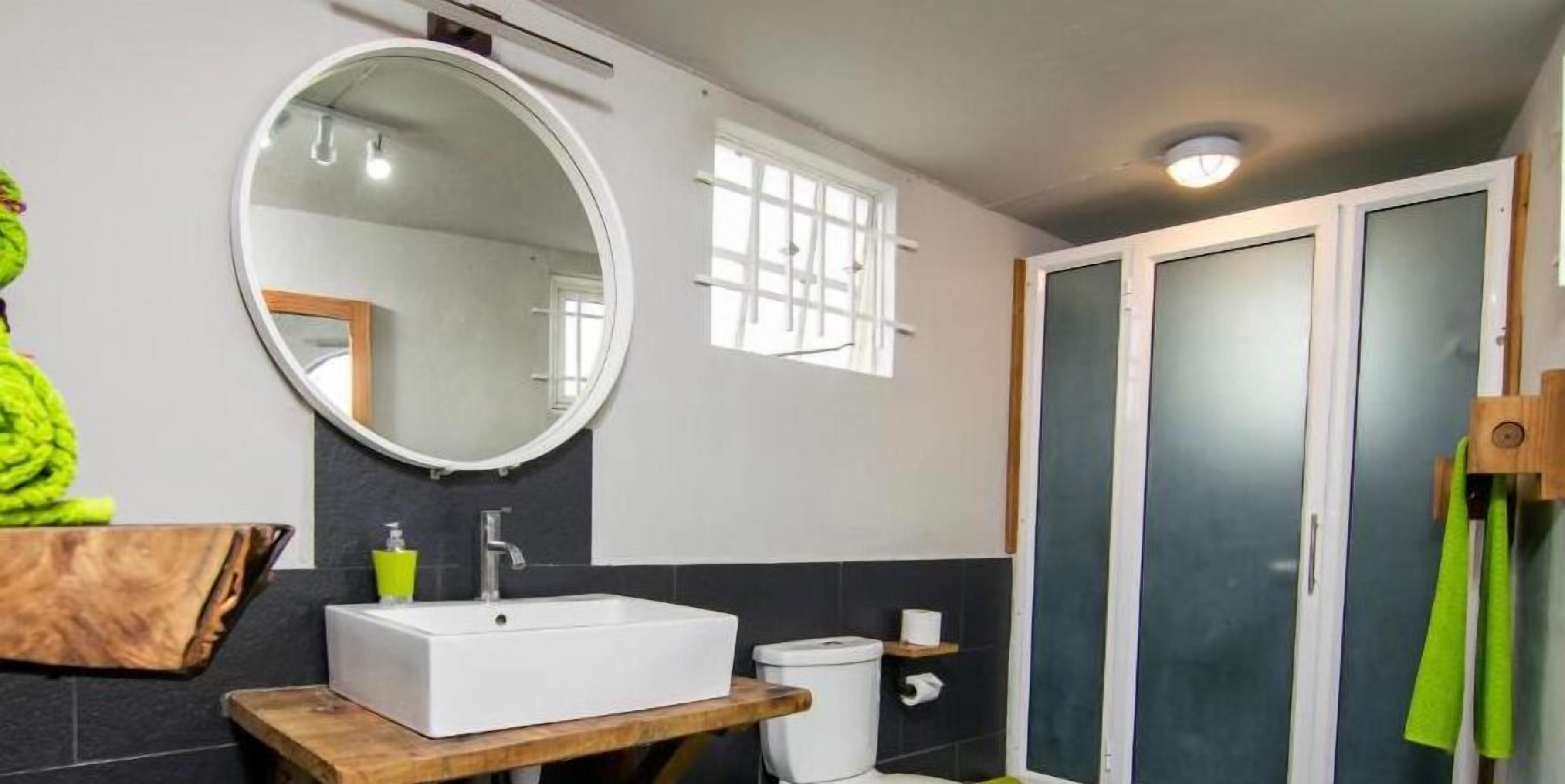A bathroom with a white sink, a round mirror, a toilet, and a shower area.