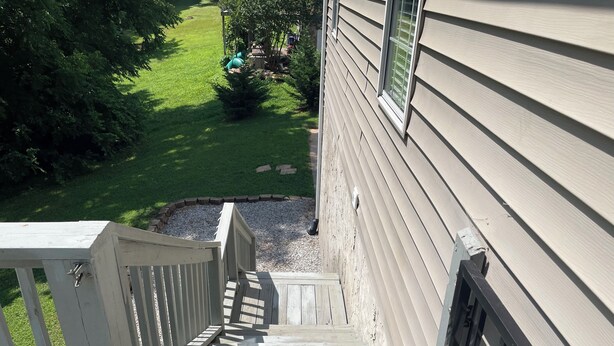 Eine Holztreppe führt zu einem Haus mit hellbeige Fassade und einem kleinen Garten.