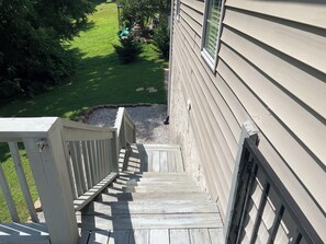 A wooden staircase leading to a house with a beige exterior and a small garden area.