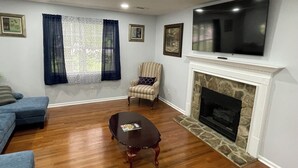 Ein Wohnzimmer mit Kamin, einem darüber montierten Fernseher, einem blauen Sofa, einem gestreiften Ohrensessel und einem Couchtisch mit einer Zeitschrift.