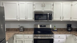 Eine moderne Küche mit weißen Schränken, Edelstahlgeräten, darunter Mikrowelle, Backofen und Kühlschrank, sowie Granitwerkplatten.