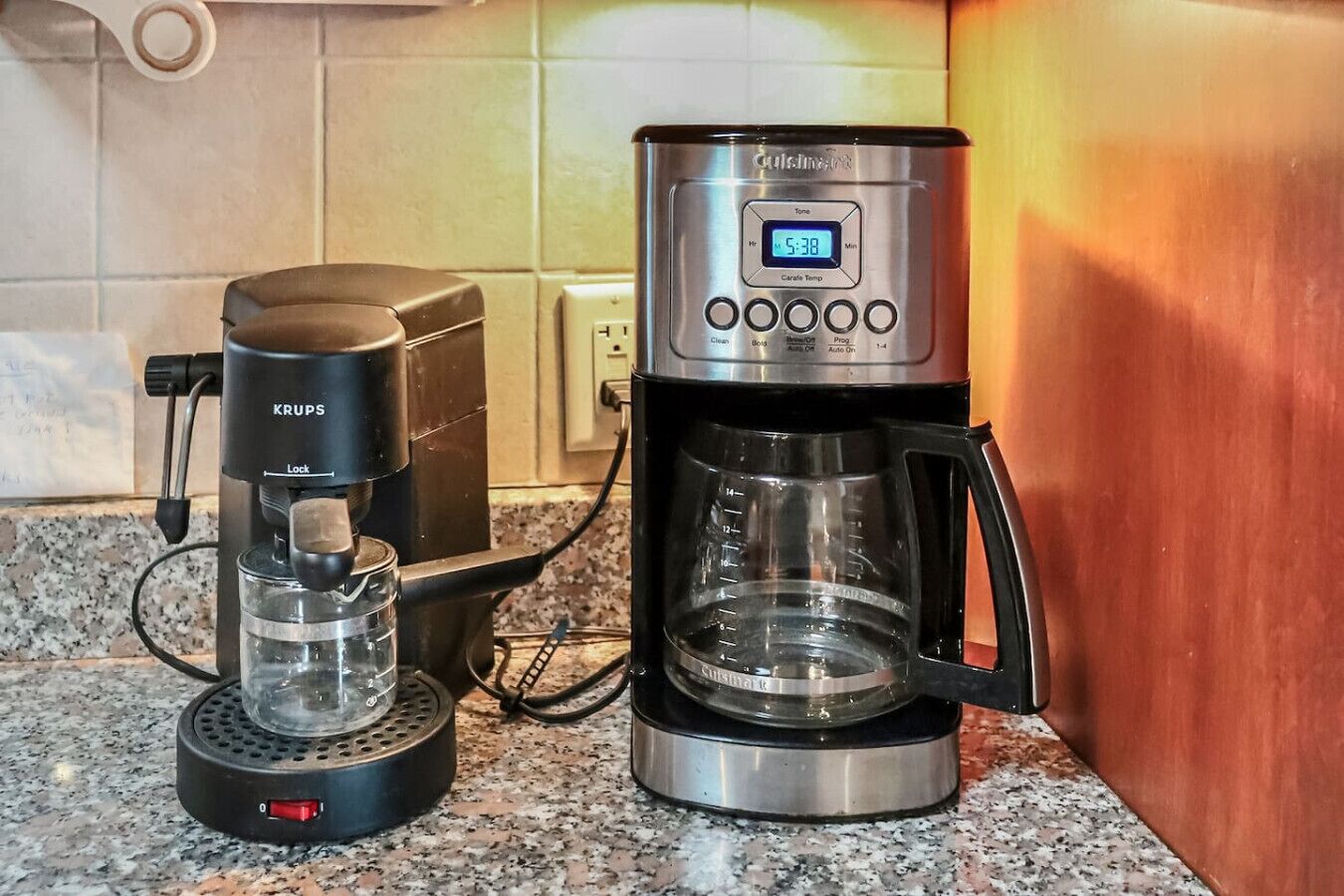 Una cafetera con pantalla digital y un molinillo de café Krups sobre una encimera de granito.