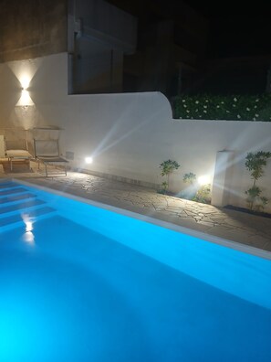 Ein Swimmingpool mit blauer Färbung, umgeben von einer weißen Mauer und kleinen Pflanzen.