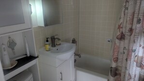 Ein Badezimmer mit einem weißen Waschbecken, einem Spiegel und einer Duschvorhang mit Fischmuster.