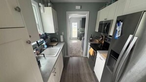 A narrow kitchen with white cabinets, a stainless steel refrigerator, and a microwave.