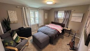 A bedroom with a bed, a chair, a guitar, and a window with curtains.