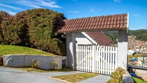 A gated entrance with a white picket fence, a tiled roof, and a view of a residential area in the background.
