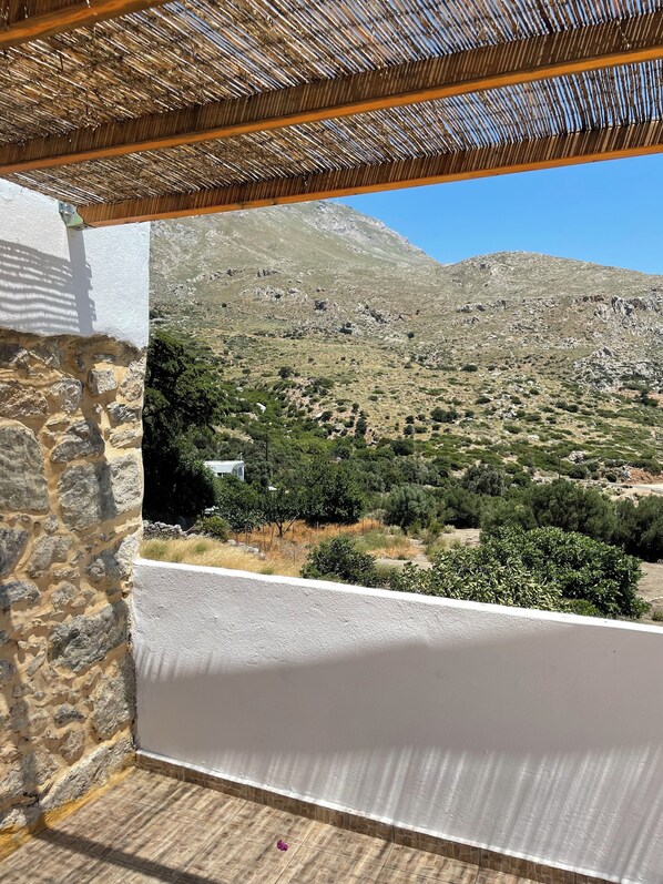 A balcony with a view of a mountainous landscape, stone walls, and a thatched roof.