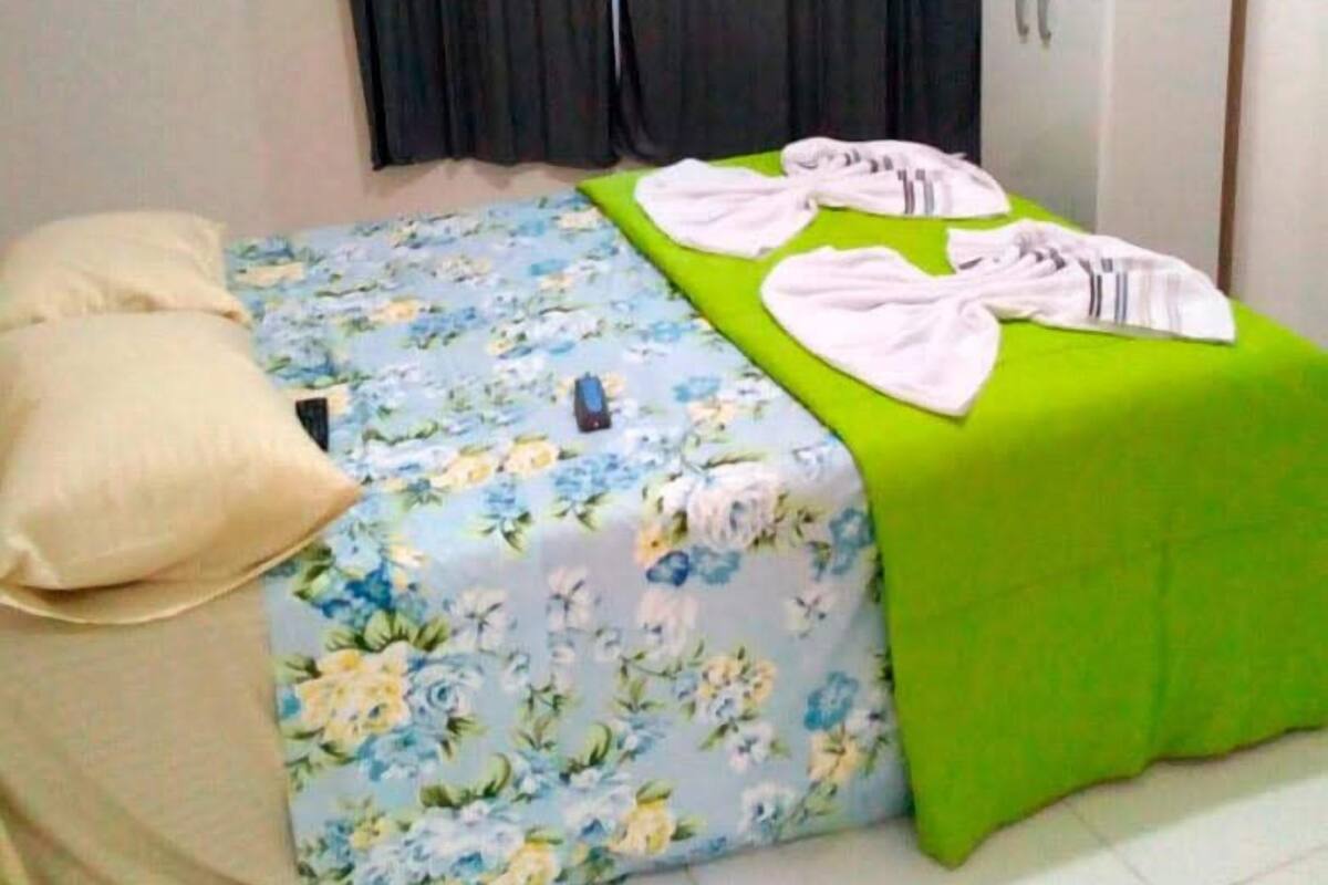 Une chambre à coucher avec une couvre-lit à motifs floraux, un coussin vert et une serviette blanche sur le lit.