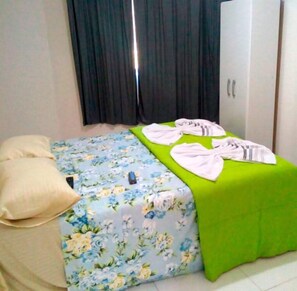 A bedroom with a floral bedspread, a green accent pillow, and a white towel on the bed. - Pousada Oluap (Mairiporã)