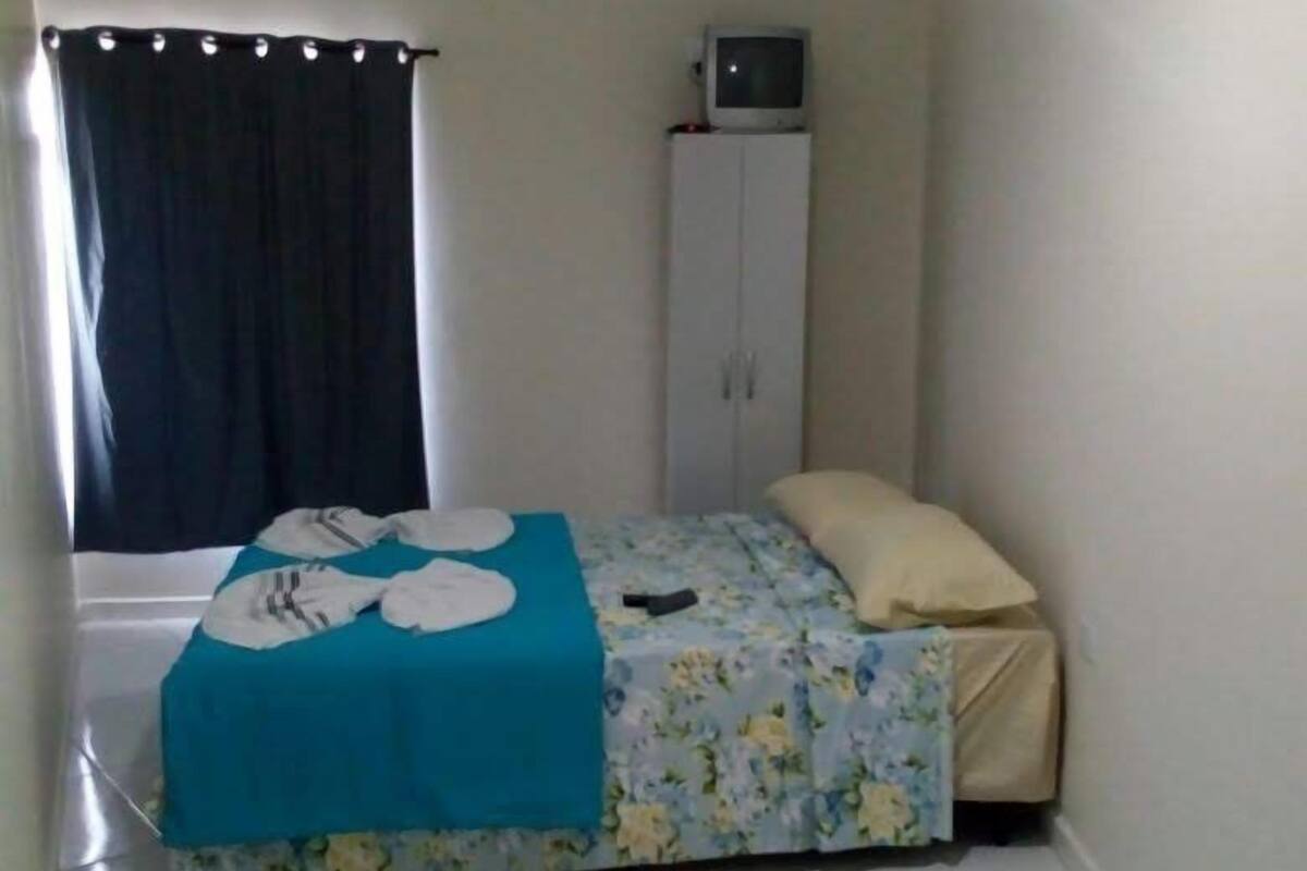 Une petite chambre avec un lit simple, une couverture bleue, une armoire blanche et une fenêtre avec des rideaux.