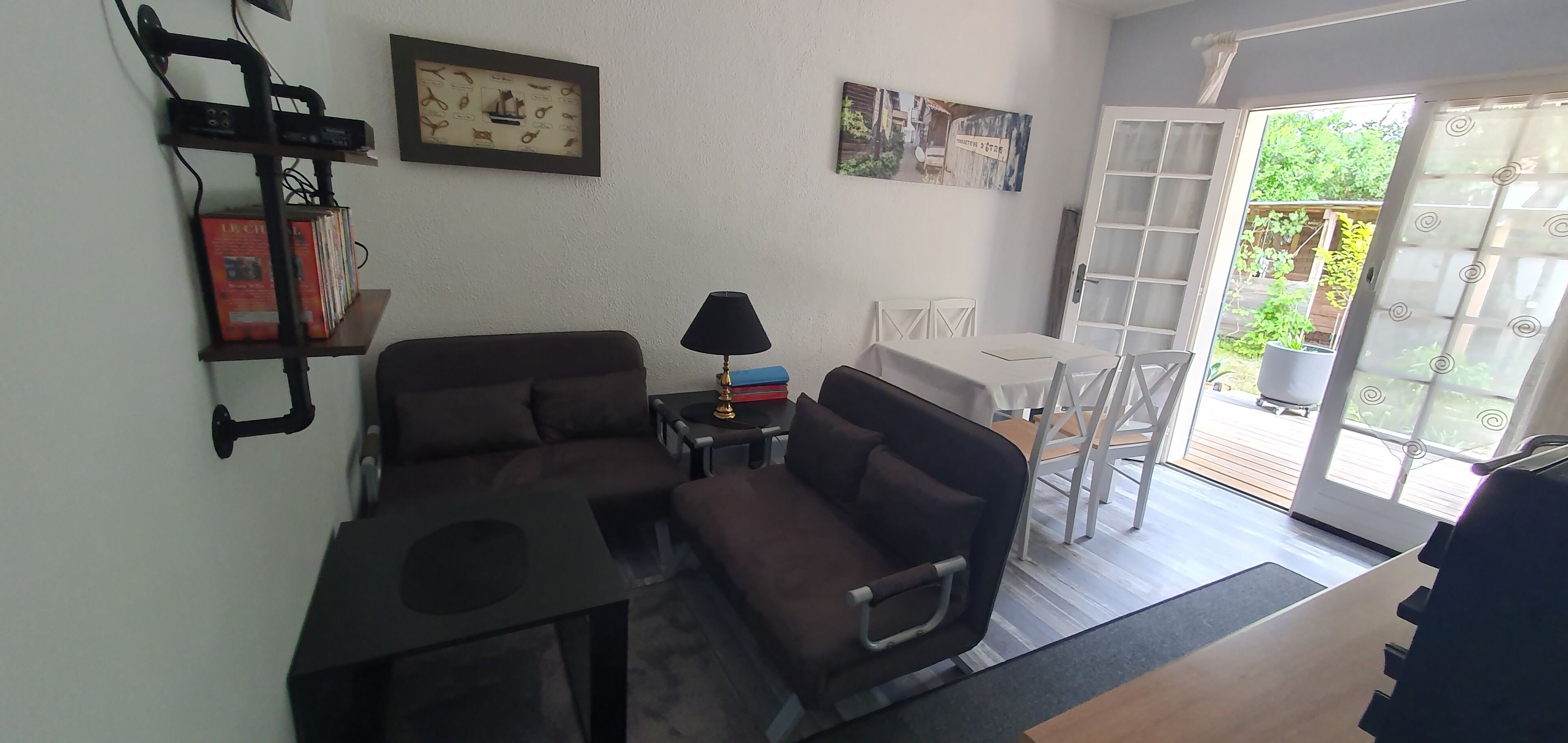 A living room with a sofa, a small table, a lamp, and a TV stand. There is a sliding glass door leading to an outdoor area.