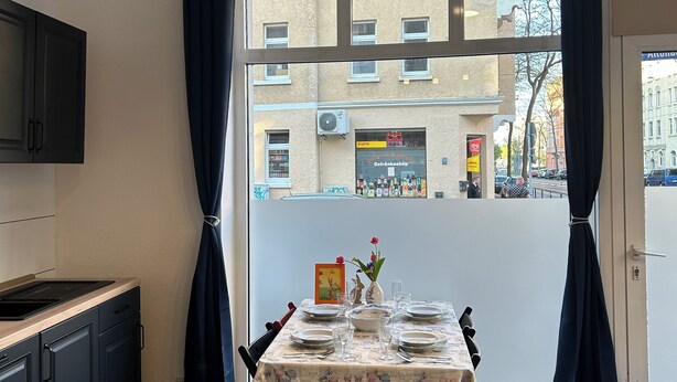 A dining area with a table set for four, a kitchen with dark cabinets, and a view of buildings outside.