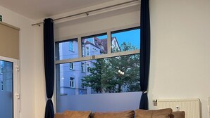 A modern living room with a large sectional sofa, a window with curtains, and a view of buildings outside.