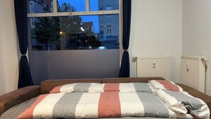 A bedroom with a bed, a window with curtains, and a radiator.