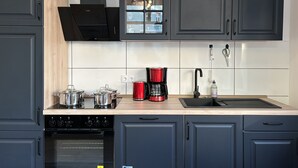 A modern kitchen with dark cabinets, a wooden countertop, a built-in oven, a coffee maker, and a sink.
