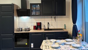 A modern kitchen with dark cabinets, a wooden countertop, and a dining area with a floral tablecloth.