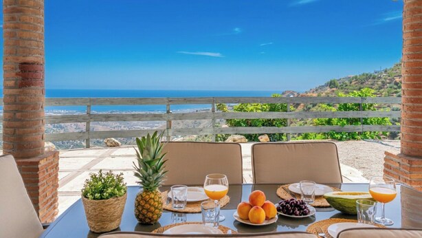 A table set for breakfast with a view of the ocean, a pineapple, and various fruits. - Casa Mirador del Mar Arenas by Ruralidays (Málaga)