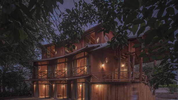 Un bâtiment en bois à plusieurs étages, doté de grandes fenêtres et d’un balcon, entouré d’arbres.