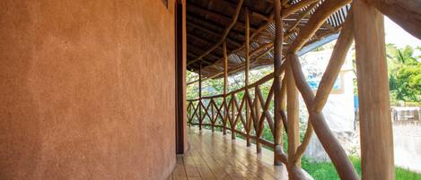 A covered wooden deck with a thatched roof, surrounded by lush greenery.