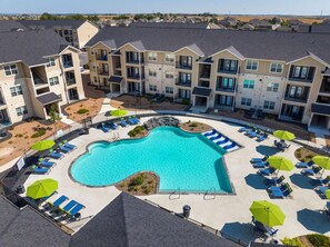 A swimming pool surrounded by lounge chairs and umbrellas, with multi-story buildings in the background. - Landing New Braunfels (New Braunfels)