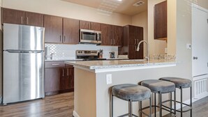 A modern kitchen with stainless steel appliances, wooden cabinets, and a granite countertop. - Landing New Braunfels (New Braunfels)
