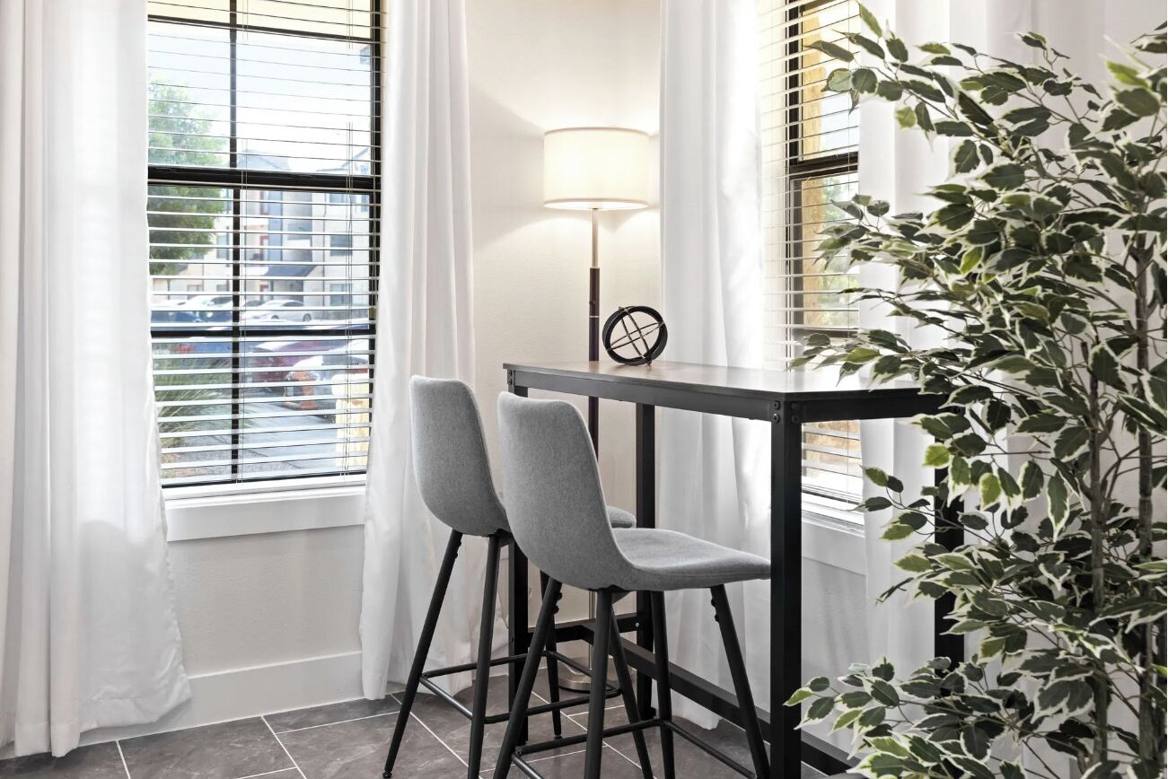 A corner room with two grey chairs, a small table, a lamp, and a potted plant.