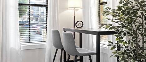 A corner room with two grey chairs, a small table, a lamp, and a potted plant.