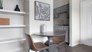 A dining area with a round table and two chairs, a kitchen with gray cabinets, and a white door. - Landing Furnished Apartments Westover Hills (San Antonio)
