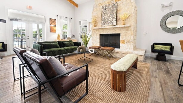 A spacious living area with a stone fireplace, leather sofas, and a large window overlooking the outdoors. - Landing Furnished Apartments Westover Hills (San Antonio)