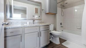 A bathroom with a toilet, sink, mirror, and shower. - Landing Furnished Apartments Westover Hills (San Antonio)