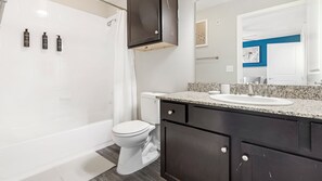 A modern bathroom with a bathtub, toilet, and vanity with a sink. - Landing South San Antonio (San Antonio)