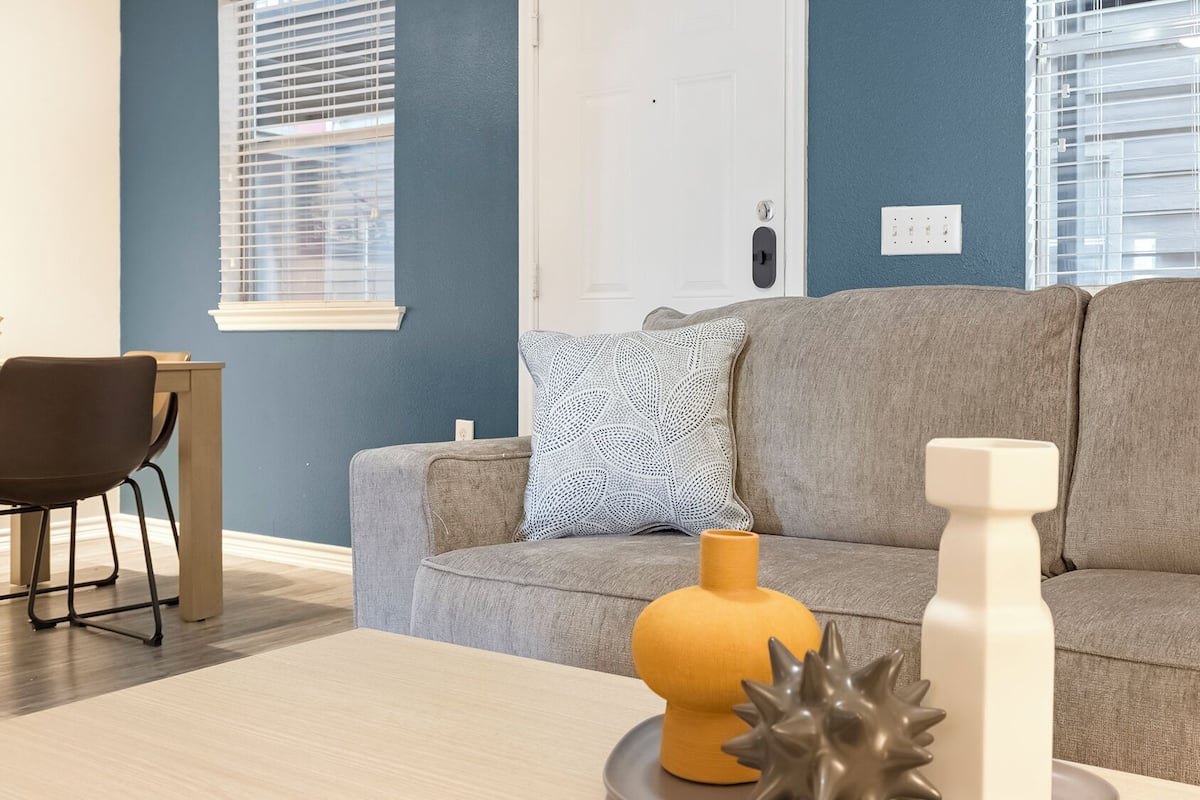 A living room with a grey sofa, a patterned throw pillow, a yellow vase, and a white vase on a coffee table.