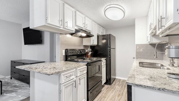 A modern kitchen with white cabinetry, a stainless steel refrigerator, a built-in oven, and a granite countertop. - Landing South San Antonio (San Antonio)
