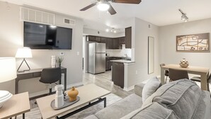 A modern living room with a sofa, coffee table, and TV. There is a kitchen area with cabinets and a refrigerator. - Landing South San Antonio (San Antonio)