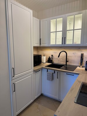 A modern kitchen with white cabinets, a black sink, and a wooden countertop.
