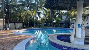 A swimming pool with a curved design, surrounded by palm trees and a thatched roof structure.