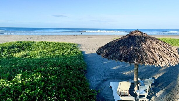 A beach with a thatched umbrella and lounge chairs.
