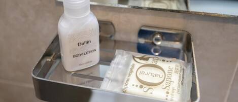 A bathroom shelf with a bottle of Dallin body lotion and a packet of Jeunet soap.