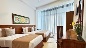 Una habitación de hotel con dos camas, un escritorio y un ventanal grande con cortinas.