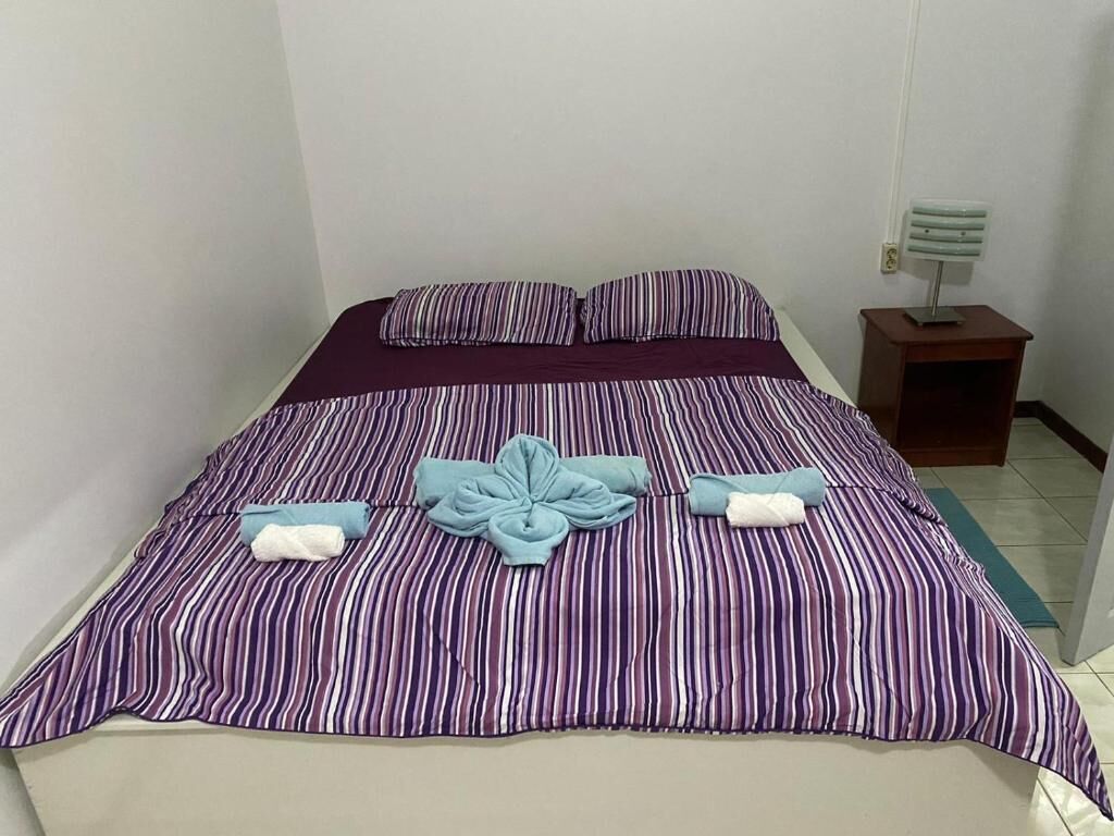 Ein ordentlich bezogenes Bett mit Streifenmuster, ein kleiner Nachttisch mit Lampe und eine Wandleuchte.