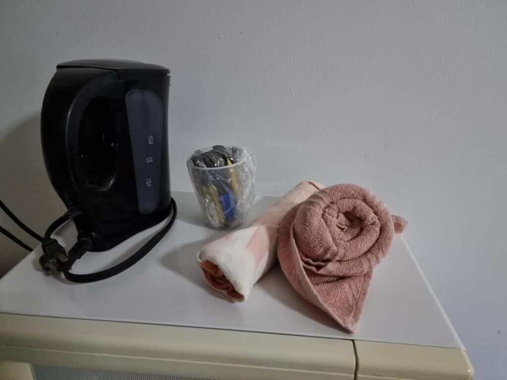 Uma cafeteira preta, um recipiente de vidro com tampa de metal e uma toalha rosa sobre uma superfície branca.